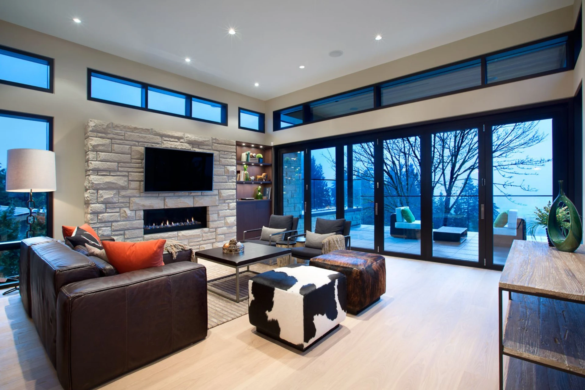 Contemporary living room with stone fireplace and floor-to-ceiling windows at dusk